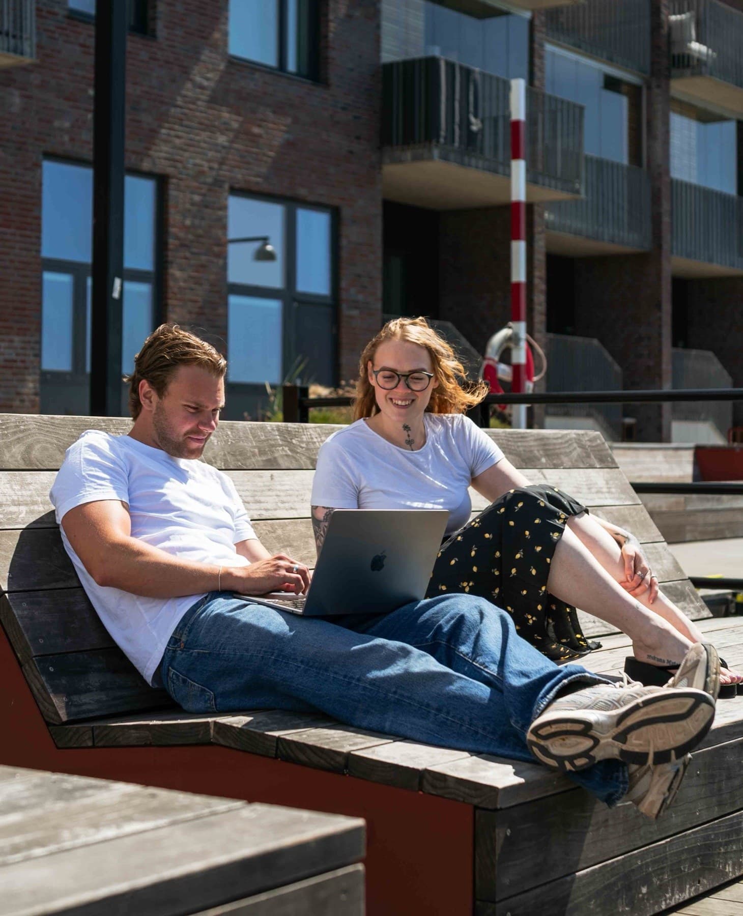 Två personer sitter vid en bank och tittar på en laptop — äkta foto kontra arkivbild